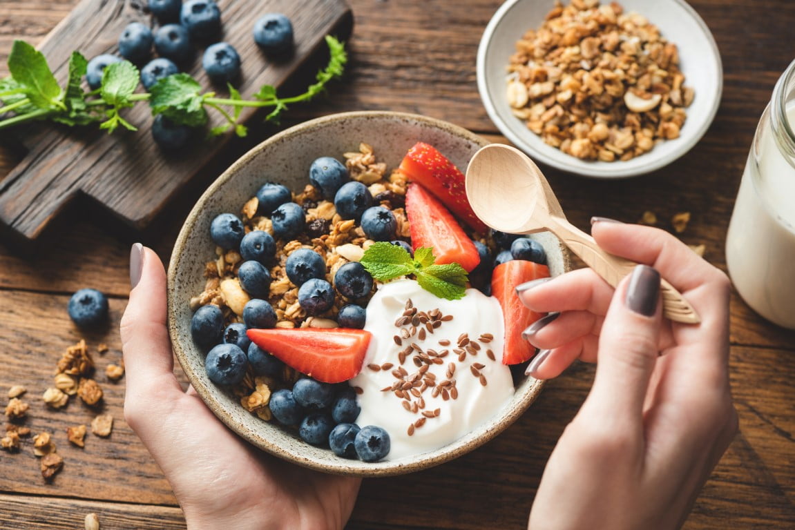 Female hand holding a spoon over a bowl of Granola With Greek Yogurt And Berries